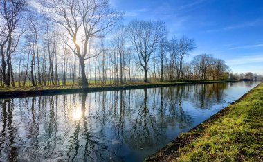 Sakin bir kanal sahnesinde kışın ağaçların cazibesi ve suda parıldayan çarpıcı yansımaları sergilenir.