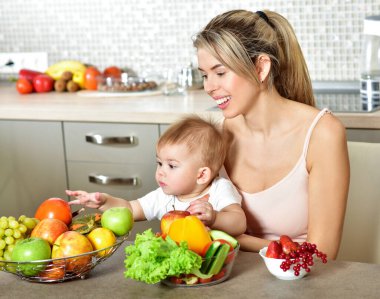 Mutfakta bebeği olan mutlu genç bir anne. Taze sebze ve meyve..