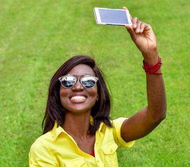 Güzel gülümseyen Afrikalı kız selfie çekiyor. Dışarıda güneş gözlüklü modacı kadın. Yeşil Çimenli Sağlıklı Gülümseyen Kız.