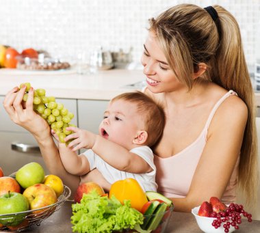Mutfakta bebeği olan mutlu genç bir anne. Taze sebze ve meyve..