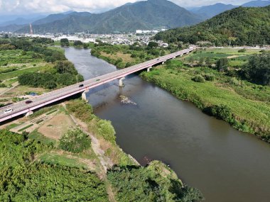 A bridge spans a river in a lush green valley. The bridge is surrounded by trees and the valley is full of greenery