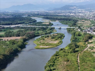 A bridge spans a river in a lush green valley. The bridge is surrounded by trees and the valley is full of greenery