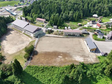 Ortasında büyük bir bina olan kırsal bir bölge manzarası. Bina bir toprak tarlası ve ormanla çevrili.