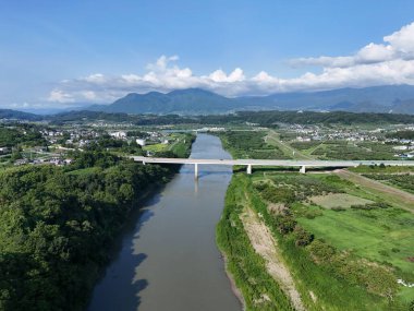 Üzerinde köprü olan bir nehir ve sağında yeşil bir alan. Gökyüzü mavi ve bazı bulutlar var.