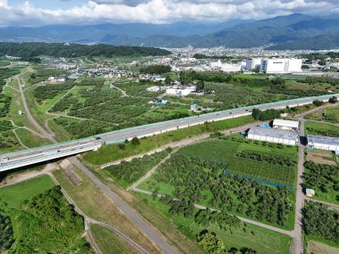Ortasında bir köprü olan yeşil ve kahverengi bir manzara. Köprü ağaçlar ve binalarla çevrili.