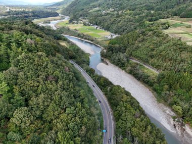 Yanı başında nehir akan bir yol. Yol arabalar ve kamyonlarla dolu. Ağaçlar yemyeşil, gökyüzü berrak