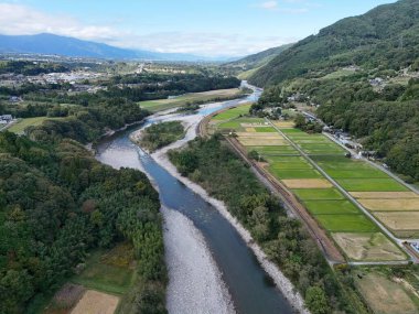 Sağ tarafında yeşil bir tarla olan bir vadi boyunca akan bir nehir. Gökyüzü açık ve manzara çok huzurlu.