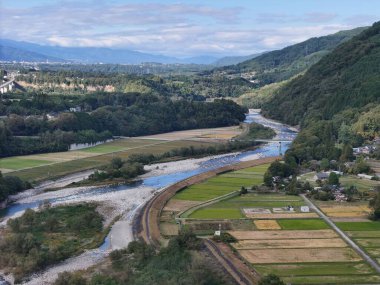 Bir nehir, sağ tarafında bir kasaba olan bir vadiden geçer. Nehir tarlalar ve dağlarla çevrili.