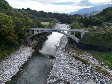 Bir köprü kayalık bir kıyı şeridine sahip bir nehri kapsar. Köprü betondan yapılmıştır ve ağaçlarla çevrilidir.