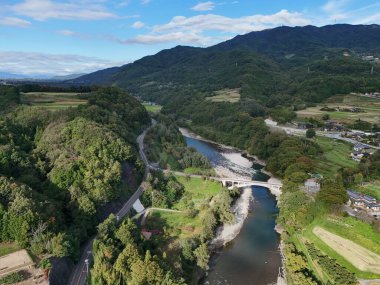 İçinden bir nehir akan güzel bir dağ sırası. Nehir yemyeşil ağaçlarla çevrili ve gökyüzü açık ve mavidir. Huzurlu ve huzurlu bir sahne.