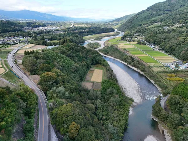 A beautiful landscape with a river running through it. The river is surrounded by trees and farmland. The sky is clear and the sun is shining