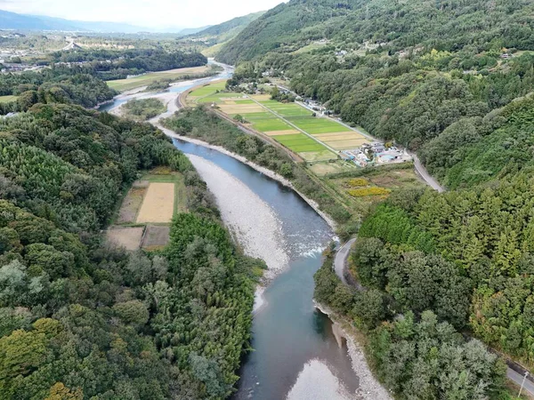 Uzakta birkaç evi olan yemyeşil bir vadiden bir nehir akıyor. Nehir ağaçlarla çevrili ve manzara huzurlu ve huzurlu.