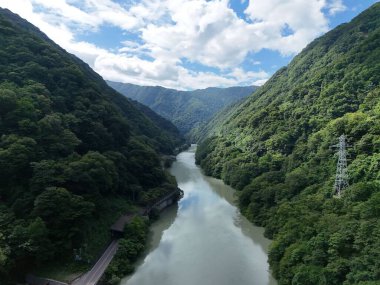 Bir nehir yemyeşil bir vadiden geçiyor. Su berrak ve sakin, etrafındaki ağaçları ve dağları yansıtıyor. Sahne huzurlu ve huzurlu.