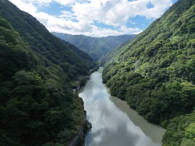 Bir nehir yemyeşil bir vadiden geçiyor. Su sakin ve berrak, etrafındaki ağaçları ve dağları yansıtıyor. Sahne huzurlu ve huzurlu.