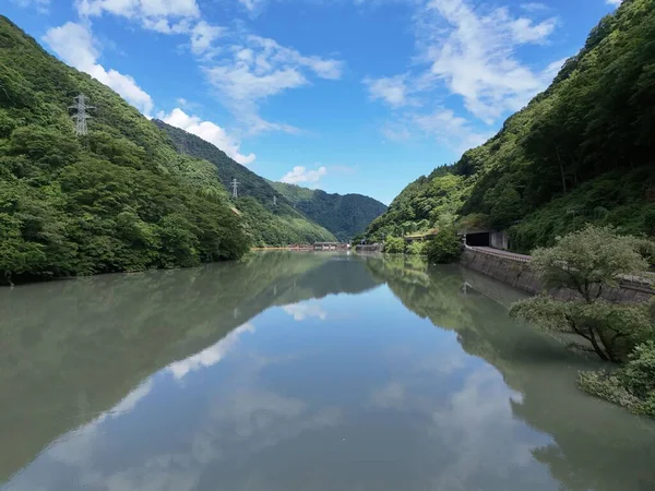 Suda dağların yansıması olan bir nehir. Gökyüzü mavi ve ağaçlar yeşil