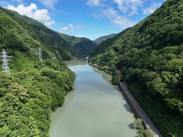 İki tarafında yeşil orman olan bir nehir. Su açık mavi bir renktir. Gökyüzü açık ve mavi