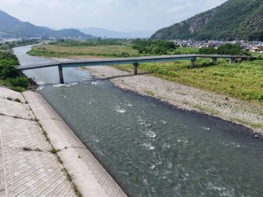 Ortasında yeşil bir köprü olan bir nehir boyunca uzanan bir köprü. Su sakin ve köprü nehrin tam ortasında yer alıyor.
