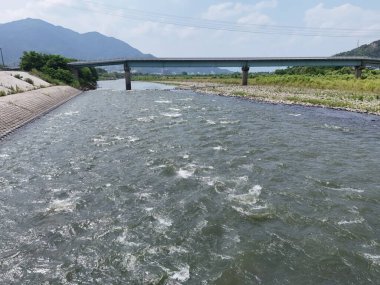 Bir köprü bir nehri bol suyla kaplar. Su dalgalı ve köprü yüksek.