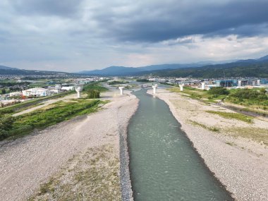 Ortasında bir köprü olan bir nehir. Gökyüzü bulutlu ve su berrak.