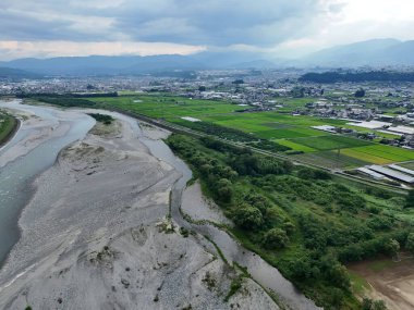 Bir nehir bir sürü yeşilliği olan bir şehrin içinden akar. Gökyüzü bulutlu ve şehir arka planda.