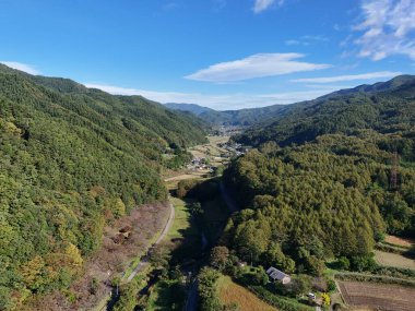 İçinden bir yol geçen güzel bir dağ sırası. Gökyüzü açık ve mavi, ağaçlar gür ve yeşil