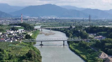 Nehir yeşil arazide akıyor, köprüler ve dağlarla.