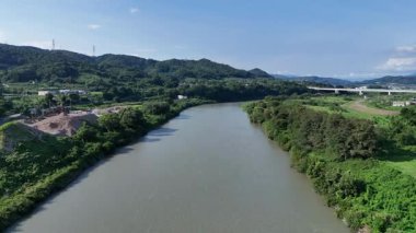 Nehir, açık mavi gökyüzünün altında, yeşil tepelerden akıyor.