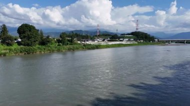 Sakin nehir mavi gökyüzünün altında bulutları ve dağları yansıtıyor.