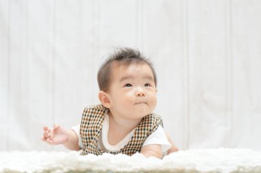 Bir bebek battaniyeye uzanıyor ve kameraya bakıyor. Bebek yelek giyiyor ve bir şeyi merak ediyor.