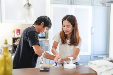Bir adam ve bir kadın mutfakta ellerini yıkıyorlar. Adam siyah gömlek giyiyor ve kadın beyaz gömlek giyiyor.