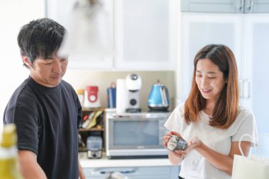 Bir adam ve bir kadın mutfaktalar, adam bir çanta tutuyor ve kadın bir yiyecek parçası tutuyor.