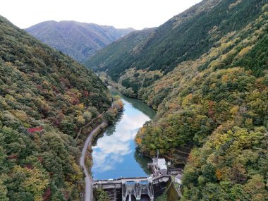 İçinden bir nehir akan güzel bir dağ sırası. Nehir ağaçlarla çevrilidir ve dağlar yapraklarla kaplıdır. Sahne huzurlu ve huzurlu.