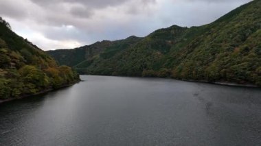 Sakin nehir bulutlu gökyüzünün altında yeşil tepeler arasında akıyor.