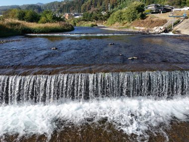 Üzerinde şelale ve köprü olan bir nehir. Su berrak ve sakin. Köprü taştan yapılmıştır.