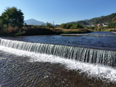 Arka planda bir dağ olan bir su akıntısı yamaçtan aşağı akar. Su berrak ve sakin, manzara huzurlu ve huzurlu.