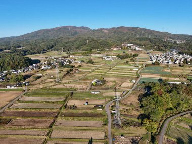 Bir sürü arazisi ve birkaç evi olan bir kırsal bölge. Gökyüzü mavi ve güneş parlıyor.