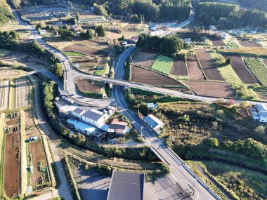 Kırsal alanda içinden geçen bir yol var. Yol tarım arazileriyle çevrili ve uzakta birkaç bina var.