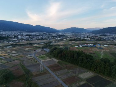 Birkaç evi ve yolu olan bir kırsal bölge. Gökyüzü bulutlu ve güneş batıyor.