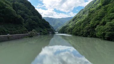 Sakin nehir dağları ve mavi gökyüzünün altındaki bulutları yansıtıyor.