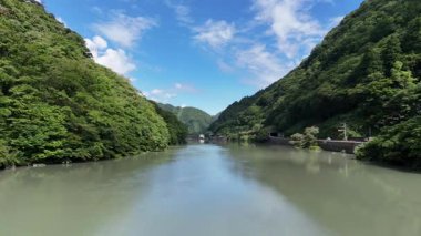 Durgun nehir mavi gökyüzünün altında yeşil dağlar arasında akıyor.