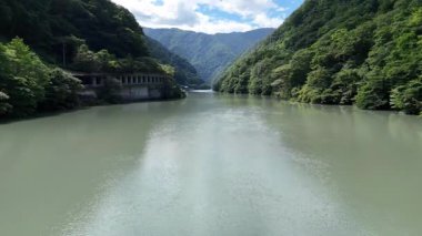 Durgun nehir mavi gökyüzünün altında yeşil dağların arasından akıyor.