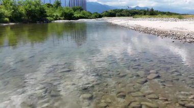 Mavi gökyüzünün altında kayalık arazide akan berrak bir nehir.