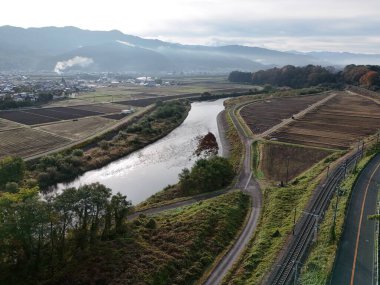 Sağ tarafında orman olan bir vadi boyunca akan bir nehir. Vadi tepelerle çevrili ve gökyüzü bulutlu.