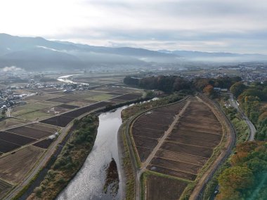Arka planda bir şehir olan bir vadi boyunca akan bir nehir. Gökyüzü bulutlu ve görüntünün havası huzurlu ve huzurlu.