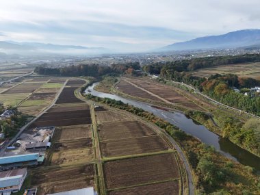 Büyük bir nehir bir mahsul tarlasının içinden akar. Gökyüzü bulutlu ve güneş görünmüyor.