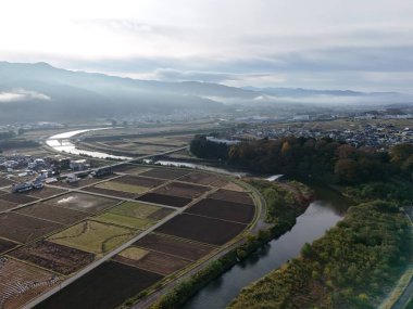 Diğer tarafında bir kasaba olan vadiden bir nehir akıyor. Gökyüzü bulutlu ve güneş bulutların arasında parlıyor.