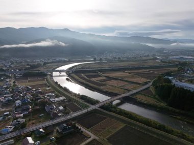 İçinden nehir akan bir şehir. Nehir evler ve binalarla çevrilidir. Gökyüzü bulutlu ve güneş batıyor.
