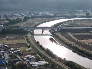 Bir nehir evleri ve köprüsü olan bir kasabadan geçiyor. Köprü nehrin üzerinde ve ağaçlarla çevrili.