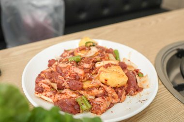 Tahta bir masada et ve sebzeli bir tabak yemek. Tabak beyaz, yemek kırmızı.