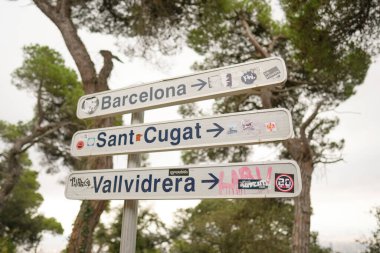 Farklı yönleri gösteren üç oklu bir işaret. Tabela çıkartmalarla kaplı ve grafiti benzeri bir görünüşü var.